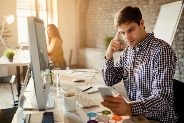 Jungunternehmer liest Nachricht auf dem Smartphone, während er im Büro arbeitet