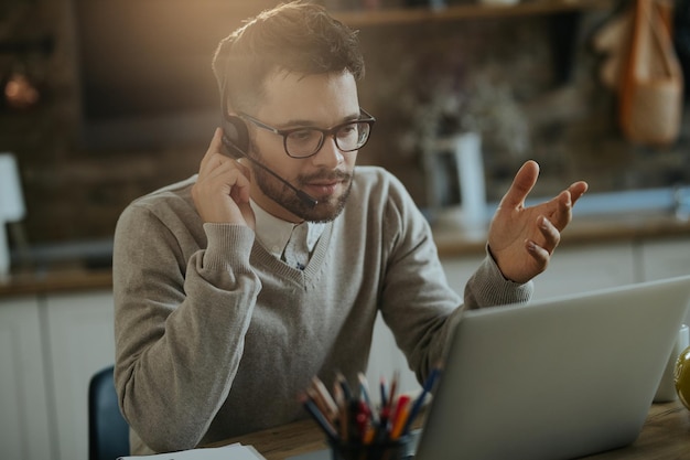 Jungunternehmer mit Telefonkonferenz über einen Computer, während er zu Hause arbeitet