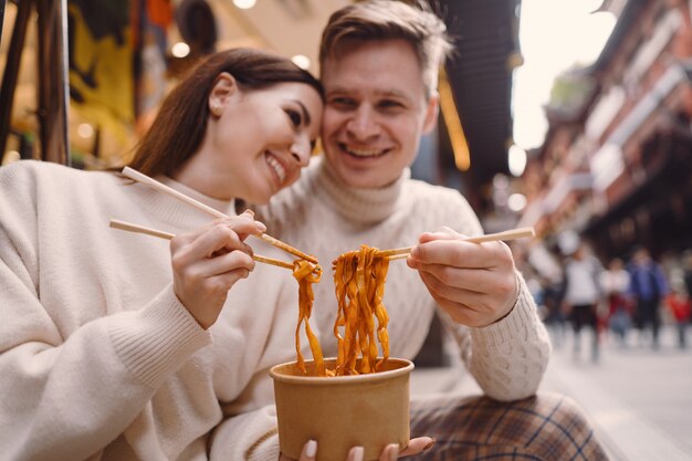 Jungvermähltenpaare, die Nudeln mit Essstäbchen in Shanghai außerhalb eines Lebensmittelmarktes essen