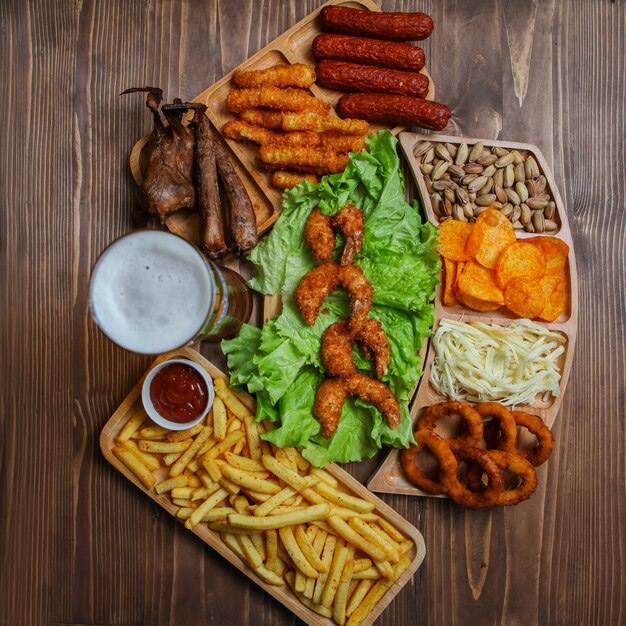 Junk-Food-Produkte in Holztellern mit Bier, Käse, Grill, Pistazien-Draufsicht