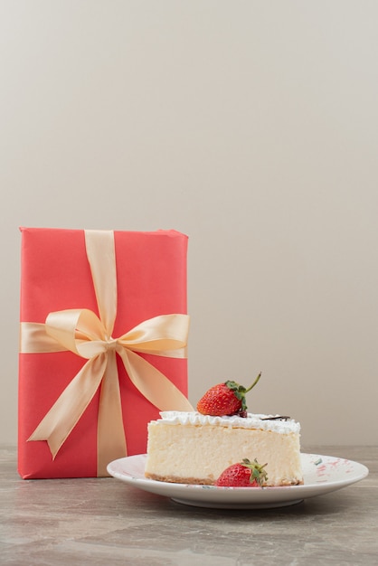 Käsekuchen mit erdbeeren und ein geschenk auf marmortisch.