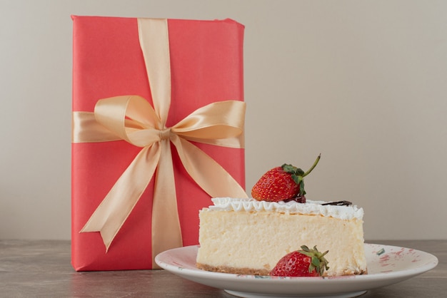 Käsekuchen mit Erdbeeren und ein Geschenk auf Marmortisch