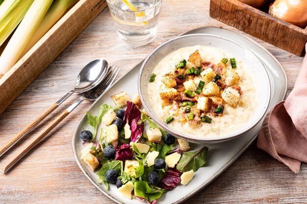 Käsige Lauchsuppe mit Croutons Speck und frischen Salatblättern auf einem Holztisch