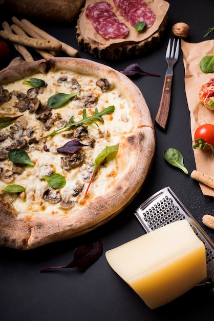 Käsige Pilzpizza mit Käse und Reibe nahe Bestandteilen über schwarzem Hintergrund