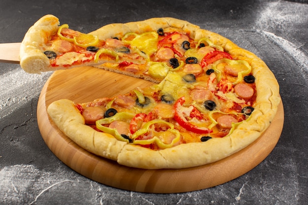 Käsige Pizza aus der Nähe mit roten Tomaten, Paprika und Würstchen aus schwarzen Oliven auf der dunklen Oberfläche