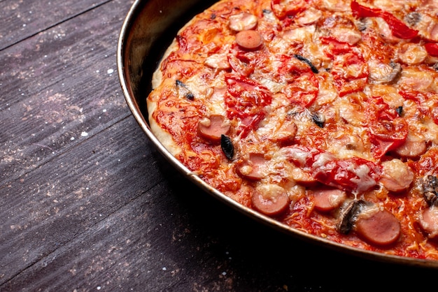 käsige Tomatenpizza mit Oliven und Würstchen in der Pfanne auf braunem Schreibtisch, Pizza Essen Mahlzeit Fast Food Käse Wurst