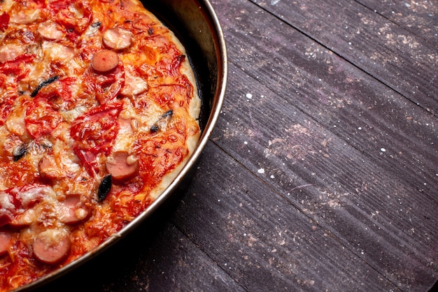 käsige Tomatenpizza mit Oliven und Würstchen in der Pfanne auf braunem Schreibtisch, Pizzamahlzeit-Fast-Food-Käsewurst