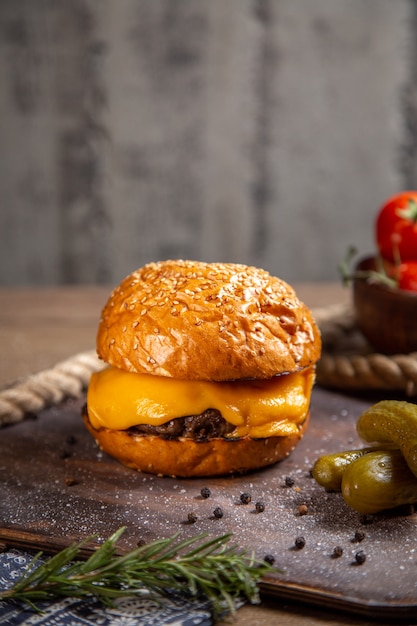 Käsiger Fleischburger der Vorderansicht mit Essiggurken, Gemüse und Tomaten auf dem hölzernen Schreibtisch