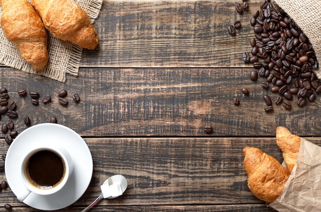 Kaffee, croissants, geröstete kaffeebohnen auf einem holzbrett mit kopierraum. mock-up für kaffeehintergrund.