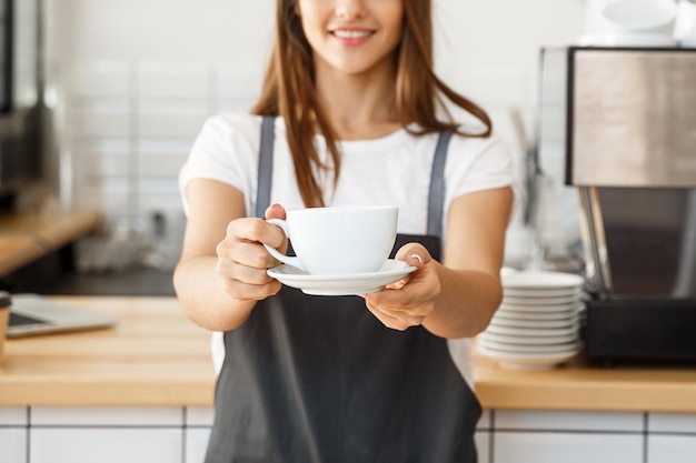 Kaffee-Geschäfts-Konzept Kaukasische Frau, die Kaffee serviert, während sie im Café steht Konzentrieren Sie sich auf weibliche Hände, die eine Tasse Kaffee platzieren
