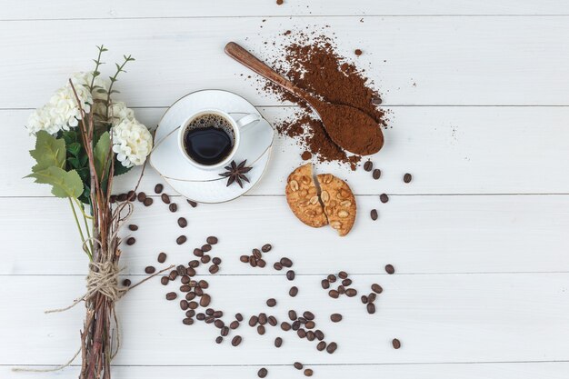 Kaffee in einer Tasse mit gemahlenem Kaffee, Gewürzen, Blumen, Kaffeebohnen, Keksen flach lag auf einem hölzernen Hintergrund