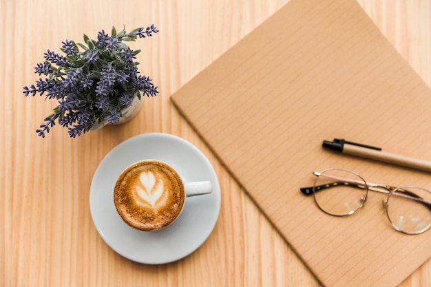 Kaffee Latte, Schreibwaren und Lavendel blühen auf hölzernem Schreibtisch