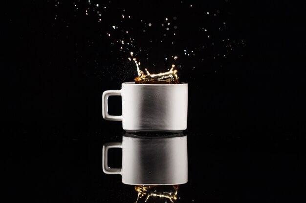 Kaffee spritzt in der weißen Schale auf schwarzem Hintergrund