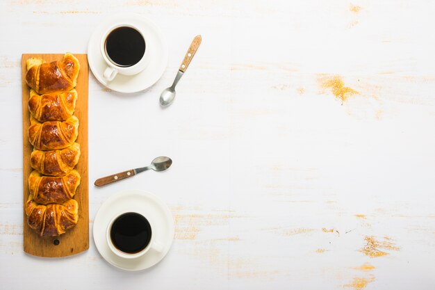 Kaffee und Löffel in der Nähe von Croissants