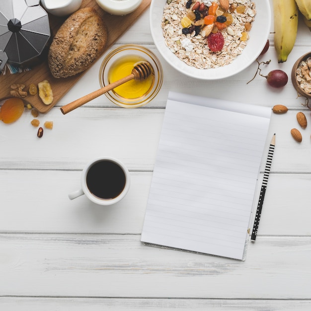 Kaffee und Notizbuch nahe Frühstückslebensmittel