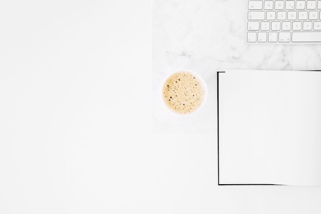 Kaffee zum Mitnehmen; leeres Notizbuch und Tastatur auf Schreibtisch gegen weißen Hintergrund