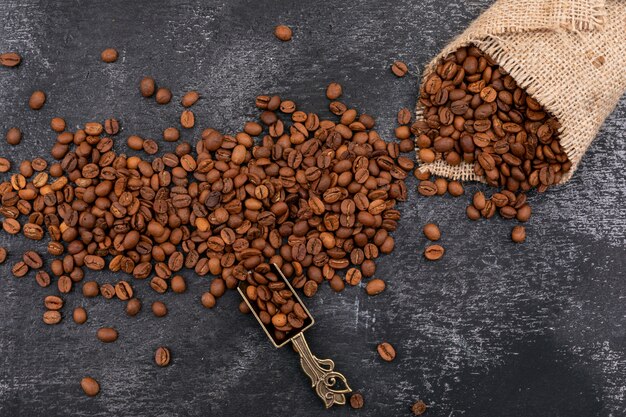 Kaffeebohnebohnen im Metalllöffel und -sackleinen auf dunkler Oberfläche