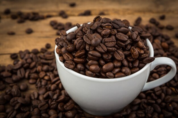 Kaffeebohnen auf einem Holztisch mit einer Tasse voll von Bohnen