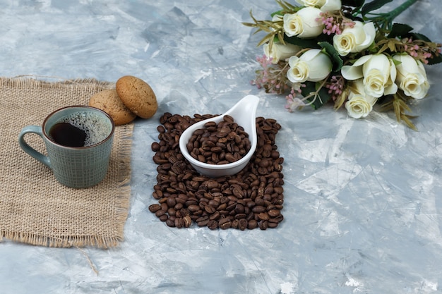 Kaffeebohnen mit hohem Blickwinkel im weißen Porzellankrug mit Keksen, Tasse Kaffee, Blumen
