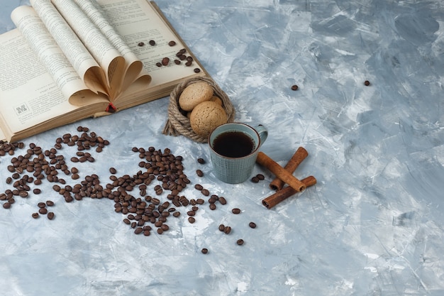 Kaffeebohnen mit hohem Blickwinkel, Tasse Kaffee mit Buch, Zimt, Kekse, Seile auf hellblauem Marmorhintergrund. horizontal