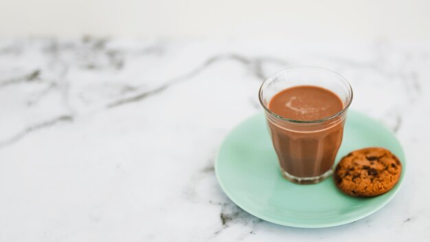 Kaffeeglas und einzelne Plätzchen auf Türkisplatte über dem Marmorhintergrund