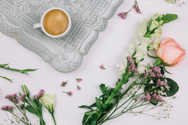 Kaffeetasse auf Tablett mit Limonium; Rose; Eustoma und Löwenmaulblume auf weißem Hintergrund