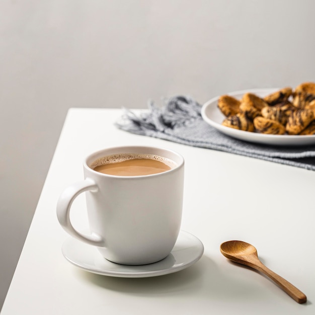 Kaffeetasse auf Tisch mit Keksen auf Teller und Löffel