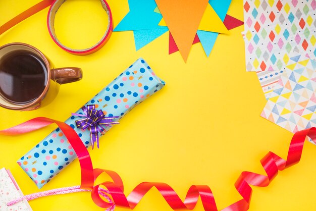 Kaffeetasse; Geschenkbox; Band und eingewickeltes Papier auf gelbem Hintergrund