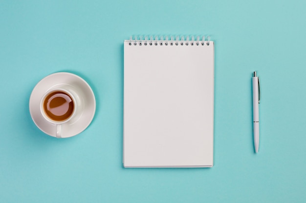 Kaffeetasse, leerer gewundener Notizblock und Stift auf blauem Schreibtisch