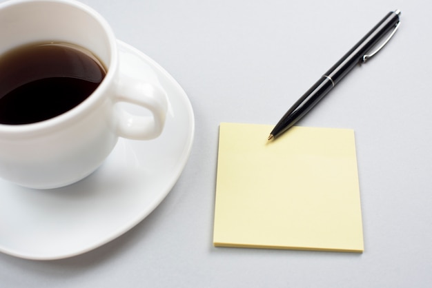 Kaffeetasse mit leerer klebender Anmerkung und Stift lokalisiert auf grauem Hintergrund