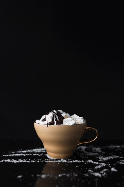 Kaffeetasse mit Schlagsahne und Schokoladensirup auf schwarzem Hintergrund