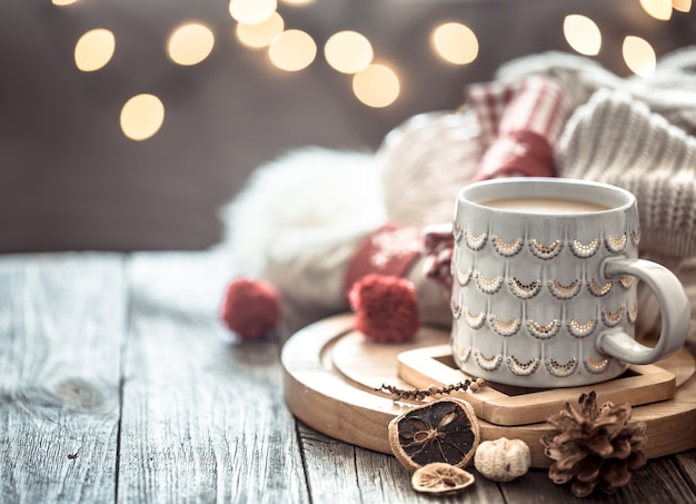 Kaffeetasse über Weihnachtslichter bokeh im Haus auf Holztisch mit Pullover an einer Wand und Dekorationen. Weihnachtsdekoration, magische Weihnachten