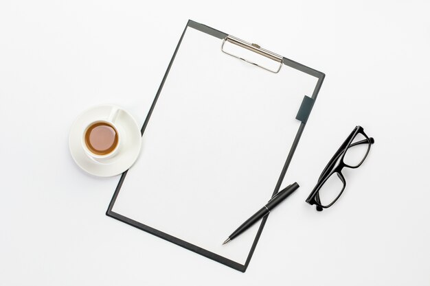 Kaffeetasse und Stift mit Weißbuch auf Klemmbrett gegen Schreibtisch