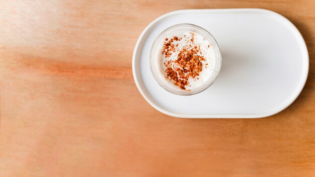 Kakaopulver über dem Kaffeeglas auf Behälter über dem braunen strukturierten Hintergrund