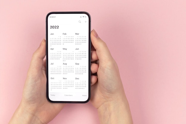 Kalender 2022. smartphone in frauenhänden. rosa hintergrund, arbeitsbereich, zu tun, konzeptfoto der planung des neuen jahres