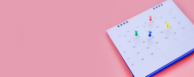 Kalender und terminplaner mit einer stecknadel auf rosa hintergrund