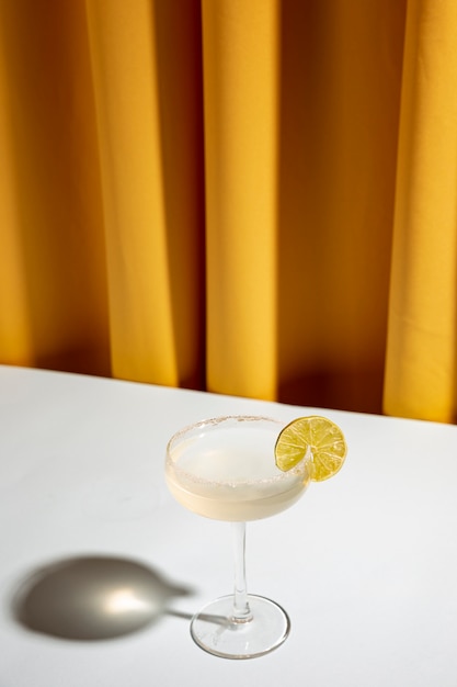 Kalkcocktail in einer Champagneruntertasse auf weißem Schreibtisch gegen gelben Vorhang