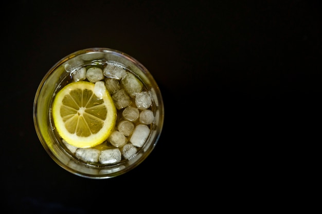 Kaltes Eistee-Glas mit Zitronenscheibe über dem schwarzen Hintergrund