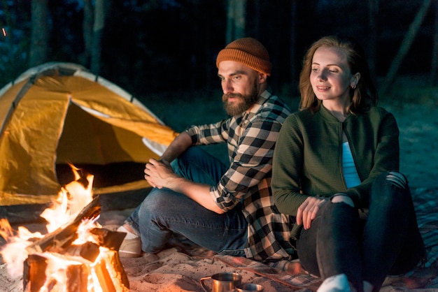 Kampierende Paare, die zusammen durch Lagerfeuer sitzen