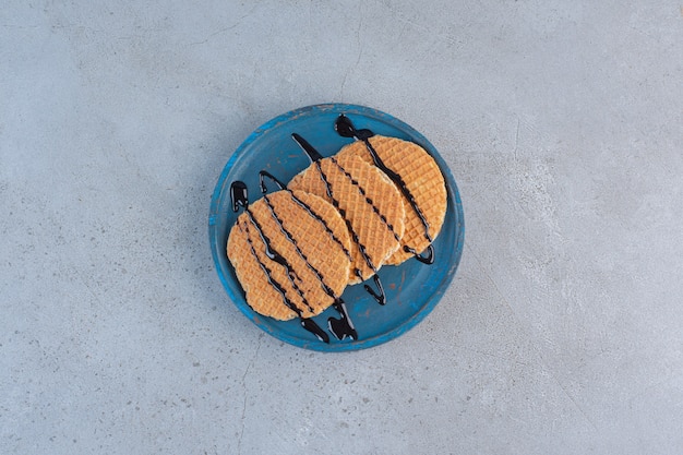 Karamellwaffeln verziert mit Schokoladensauce auf blauem Teller.