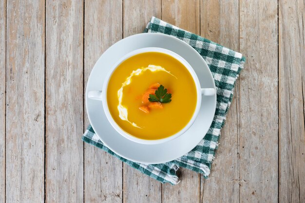 Karottensuppe mit Sahne und Petersilie auf Holztisch Nahaufnahme