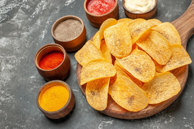 Kartoffelchips Gewürze und Mayonnaise mit Ketchup auf Holzschneidebrett auf grauem Tisch