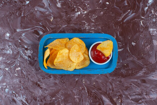 Kartoffelchips mit Ketchup in einem Holzteller auf Marmor.