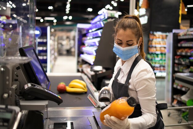 Kassiererin im Supermarkt mit Maske und Handschuhen, die vollständig gegen das Koronavirus geschützt sind