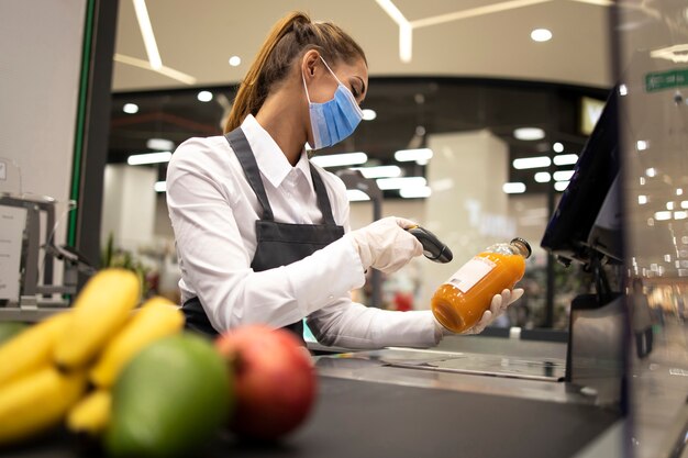 Kassiererin im Supermarkt mit Maske und Handschuhen, die vollständig gegen das Koronavirus geschützt sind