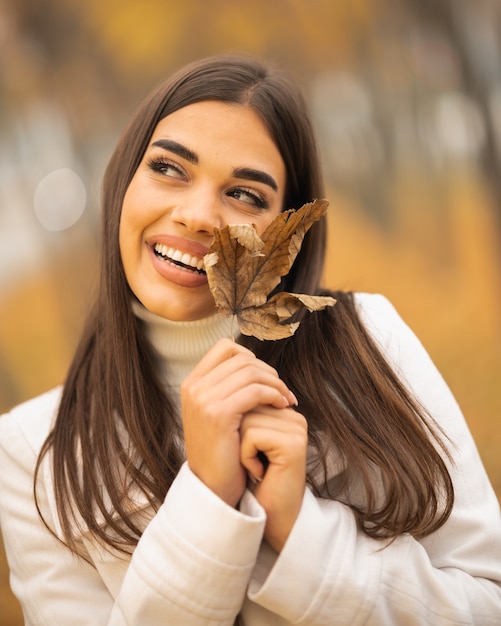 Kaukasische attraktive frau, die im herbst ein gefallenes blatt lächelt und hält