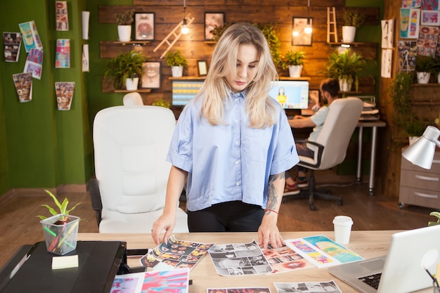 Kaukasische Designerin, die ihre Praktikantenentwürfe überprüft. Mann, der im Hintergrund an Laptop arbeitet.