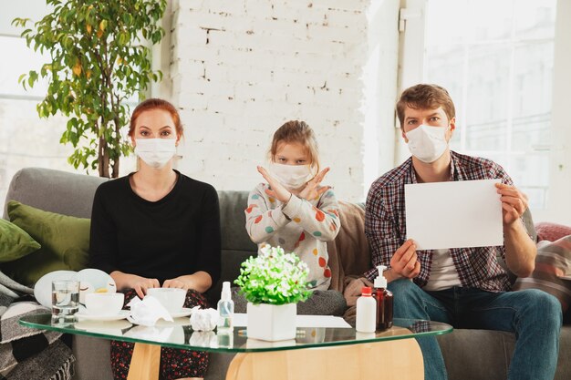 Kaukasische Familie in Gesichtsmasken und Handschuhen, die zu Hause mit Coronavirus isoliert sind