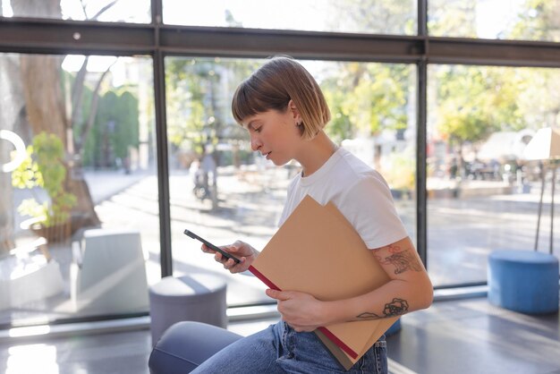 Kaukasische Frau, die das Notizbuch hält, das Telefon betrachtet