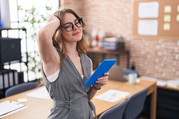 Kaukasische Frau, die im Büro arbeitet und eine Brille trägt, lächelt selbstbewusst, berührt das Haar mit der Hand nach oben und posiert attraktiv und modisch